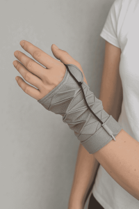 A close-up of a person wearing a modern wrist orthosis inspired by Kresling origami, featuring foldable fabric panels and a tendon-like actuator for flexible, personalized wrist support.